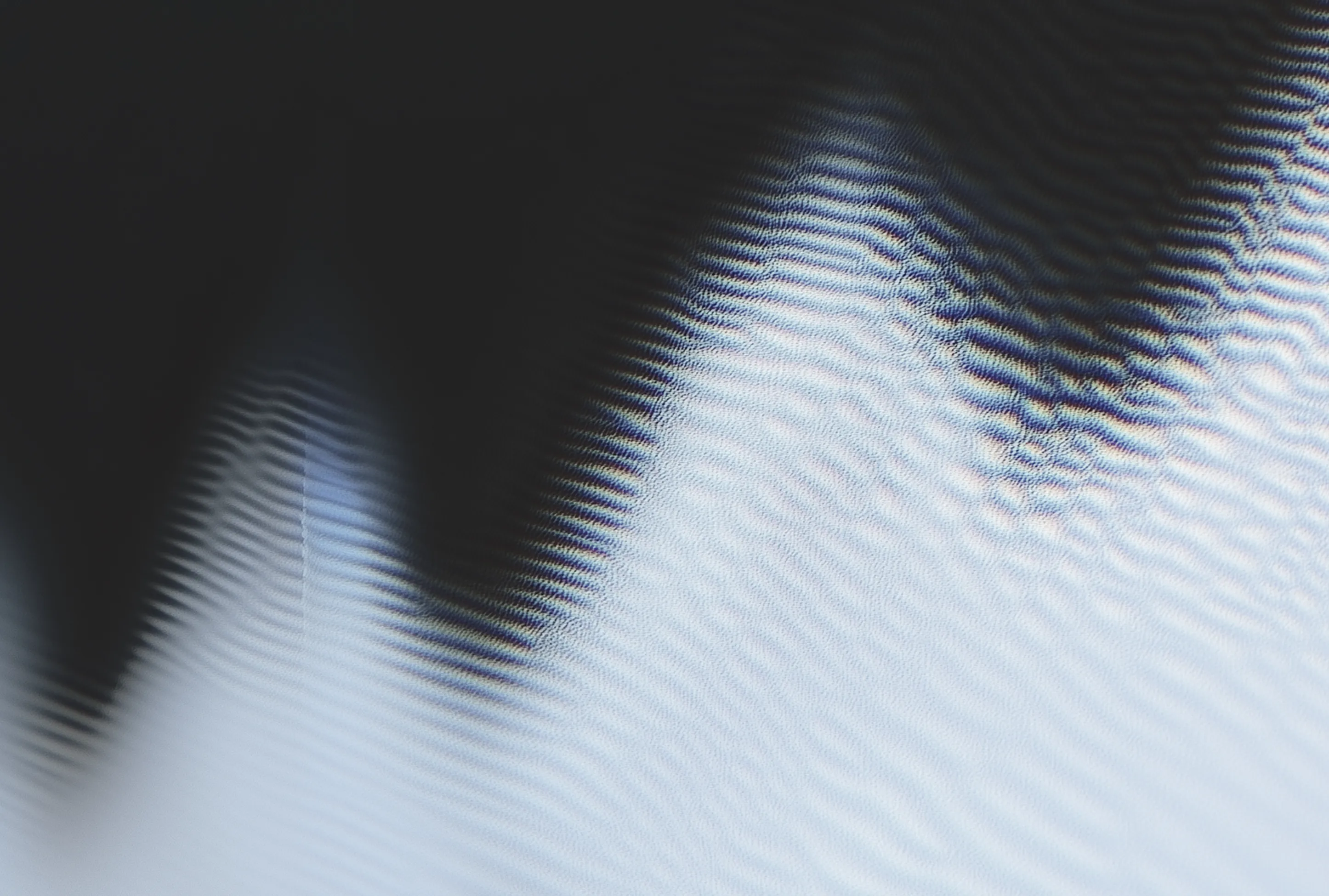 Close-up of light and shadow creating wavy, rippled patterns on a surface with a gradient from dark to light gray.